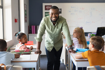 Portrait of african american young male teacher standing by multiracial elementary students in class
