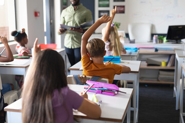 Multiracial students raising hand while african american young male teacher teaching in classroom