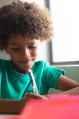Close-up of smiling african american elementary schoolboy holding pen while sitting at desk in class