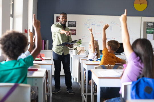African american young male teacher pointing caucasian elementary girl with hand raised in class