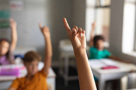 Multiracial elementary school students with hands raised during class in classroom