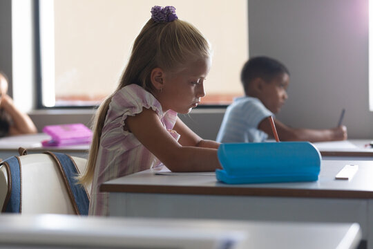 Multiracial elementary school students studying at desk in classroom