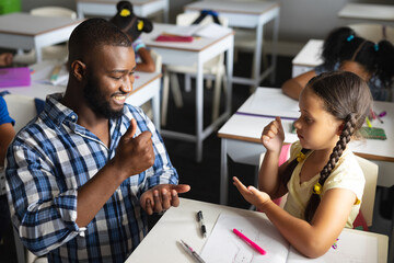 African american young male teacher teaching sign language to caucasian elementary girl in class