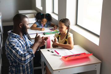 African american young male teacher communicating in sign language with caucasian elementary girl