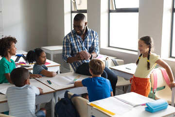 Fototapeta premium Happy multiracial elementary students looking at multiracial young male teacher showing brain model