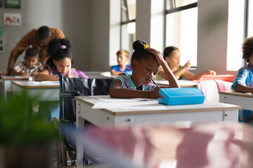 Multiracial elementary school students studying at desk in classroom - obrazy, fototapety, plakaty