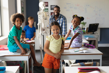 Portrait of multiracial students and african american young male teacher with skeleton in class - Powered by Adobe