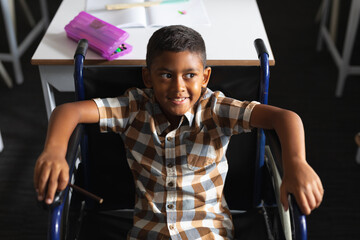 High angle view of smiling biracial elementary boy sitting on wheelchair in classroom
