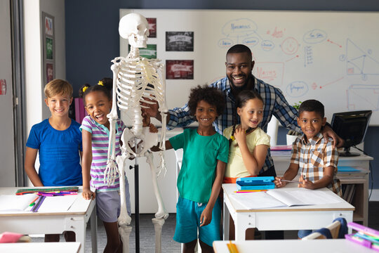 Portrait of smiling multiracial students and african american young male teacher with skeleton