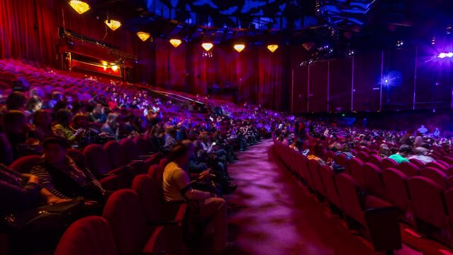 Spectators gather in the auditorium and watch the show in theatre timelapse. Large hall with red armchairs seats. Viewers filling places until turn off the light. Panoramic view from left side
