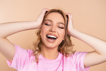 excited woman touching head while laughing with closed eyes isolated on beige.