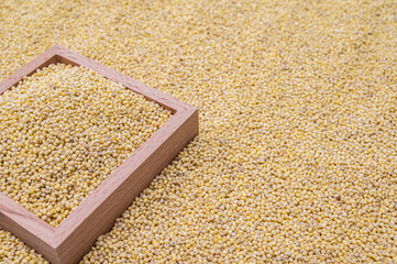 A background with millet stacked and a wooden bowl containing millet.
