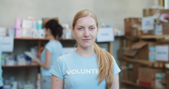 Portrait of smiling female volunteer looking at camera while posing in warehouse of food bank. Attractive female helping people in need while working at charity fund.