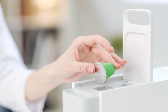 A woman holds coffee capulas in her hands and prepares espresso in a capsule coffee machine. White background. A bright room.