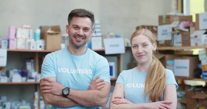Caucasian male and female volunteers in blue t-shirt standing with crossed arms and looking at camera in charitable fund. Portrait of positive group of food bank workers.