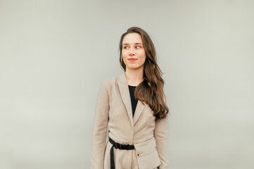 Cute lady in a beige suit stands on a beige background and looks away with a sarcastic smile on her face. Copy space