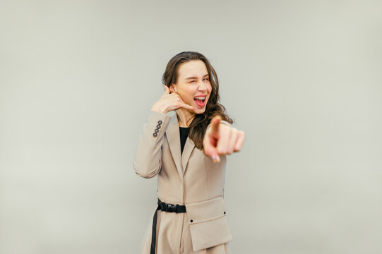 Attractive woman showing call gesture and showing finger to camera winking on beige background