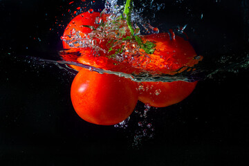 Fresh red tomato falling into water with water splash and air bubbles isolated on black background