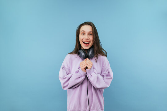 joyful lady in headphones around her neck and casual clothes looking at camera with happy face, isolated on blue background.