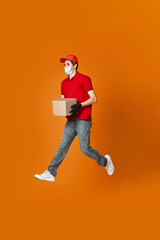 Fototapeta na wymiar Delivery man in face mask holding cardboard box and jumping