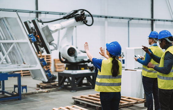 Multiethnic engineers using futuristic augmented reality glasses inside robotic factory - Industrial and technology concept - Focus on senior woman hat