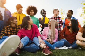 Multiethnic diverse people having fun outdoor sitting on grass at city park - Soft focus on gay man...