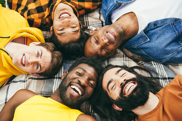 Happy diverse male friends having fun lying together in circle outdoor - Soft focus on blond man - Powered by Adobe