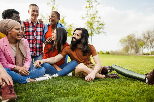 Multiethnic diverse people having fun outdoor sitting on grass at city park - Main focus on arabian girl face