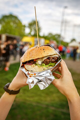 Big burger in hands at street food outdoor festival