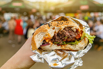 Big burger in hands at street food outdoor festival