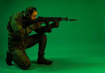 the soldier stands on one knee, takes aim, shoots. Studio. green background