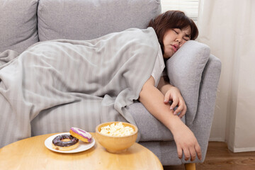 Lazy Overweight Woman Sleep on the Couch with Doughnuts and Popcorns in Front of Her - obrazy, fototapety, plakaty