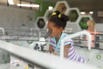 African american elementary schoolgirl looking in microscope during science practical in laboratory