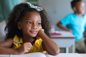 Close-up of thoughtful african american elementary schoolgirl sitting at desk in classroom