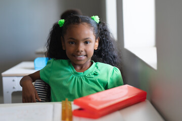 Portrait of smiling confident african american elementary schoolgirl in green dress sitting at desk