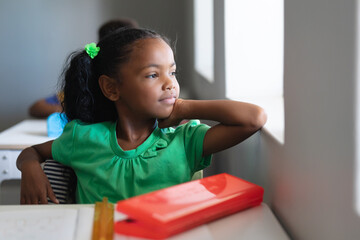 Thoughtful african american elementary schoolgirl looking through window while sitting in class