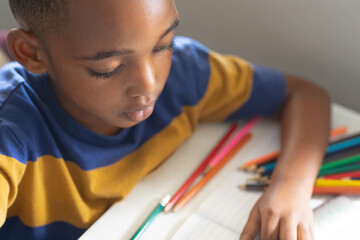 High angle view of african american elementary schoolboy drawing on book at desk in classroom