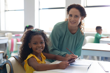 Portrait of smiling african american elementary girl with caucasian young female teacher in class