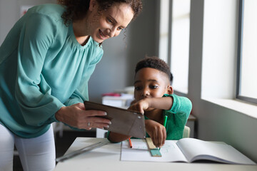 Obraz premium Caucasian young female teacher teaching on digital tablet to african american elementary boy