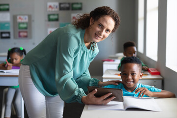 Obraz premium Portrait of caucasian young female teacher with african american elementary schoolboy at desk