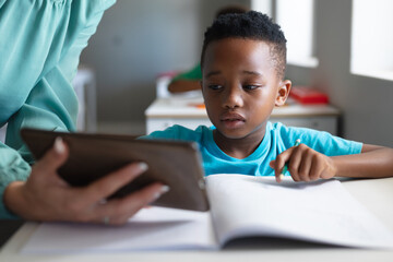 Close-up of caucasian young female teacher showing digital tablet to african american elementary boy