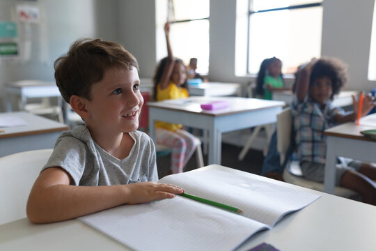 Smiling caucasian elementary schoolboy looking away while sitting at desk in classroom