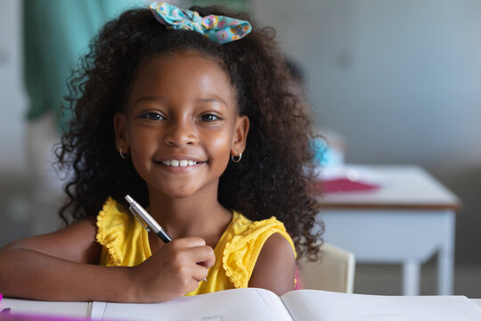 Portrait of smiling african american elementary schoolgirl with curly hair sitting at desk in class