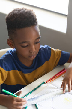 High angle view of african american elementary schoolboy drawing line on book at desk in classroom