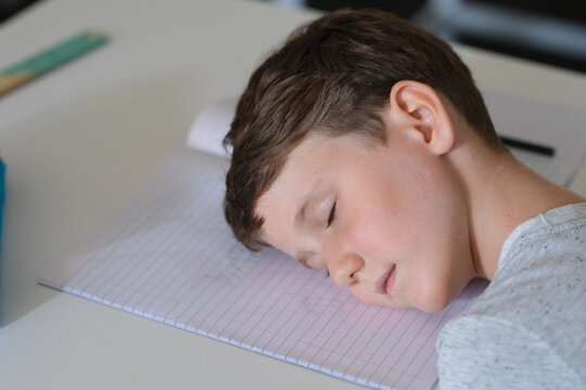 Close-up of caucasian elementary schoolboy sleeping on book at desk in classroom