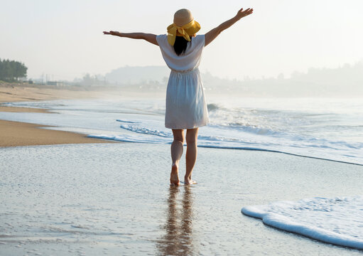 Happy woman standing on the beach with hands up.