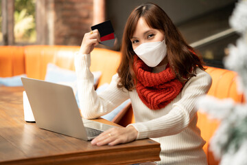Woman with white sweater and scarf shopping online by using credit card for transitioning payments to shops or malls during snowing in Winter at home by using laptop to select product and move to cart