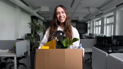 A young woman is holding a cardboard box with personal belongings. New job in the office