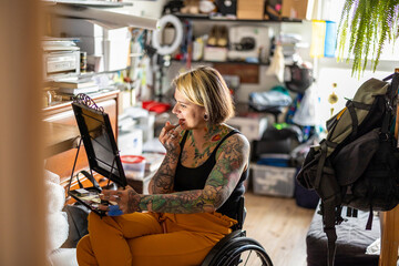 Naklejka na ściany i meble Young woman in a wheelchair doing her make-up at home 