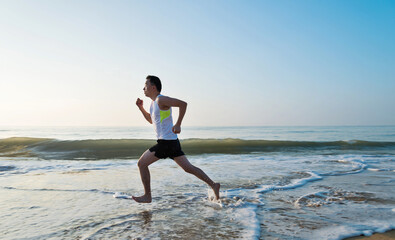 Fototapeta na wymiar Young man running along beach in the morning